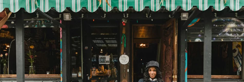 Portrait of confident young black woman standing at a vibrant, colorful cafe entrance in the city.